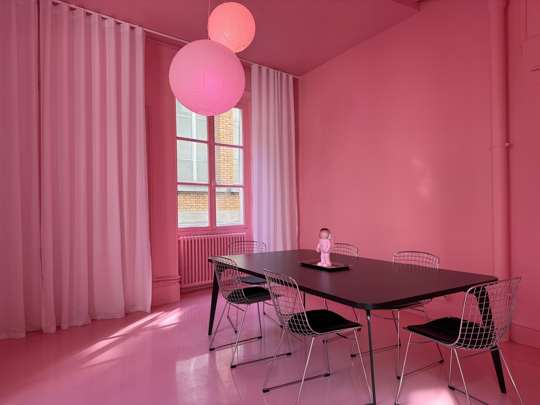 Black table and Bertoia chairs in the all-pink room with designer pendant lights