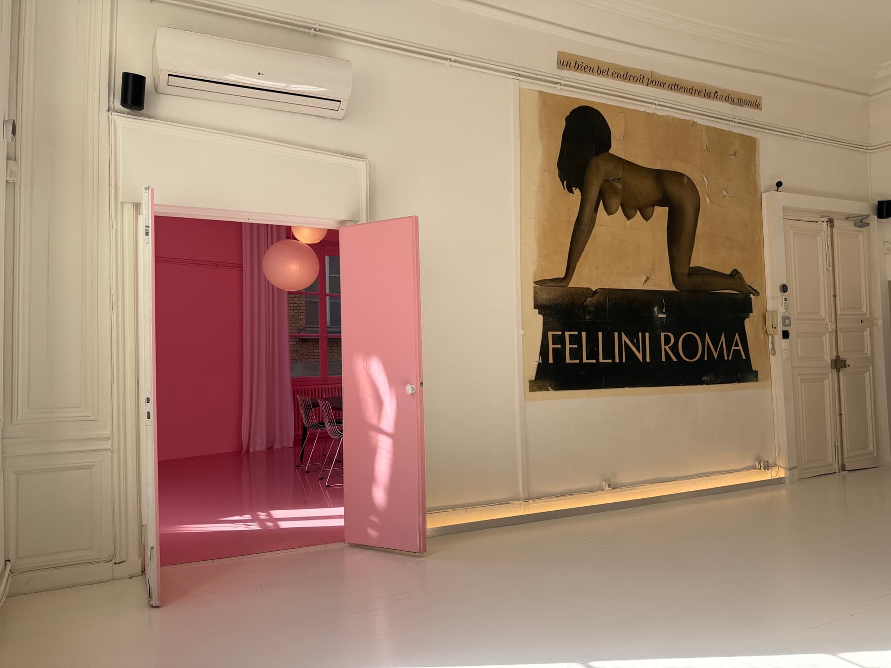 Pink room entrance from the main space — pink door and Fellini Roma poster