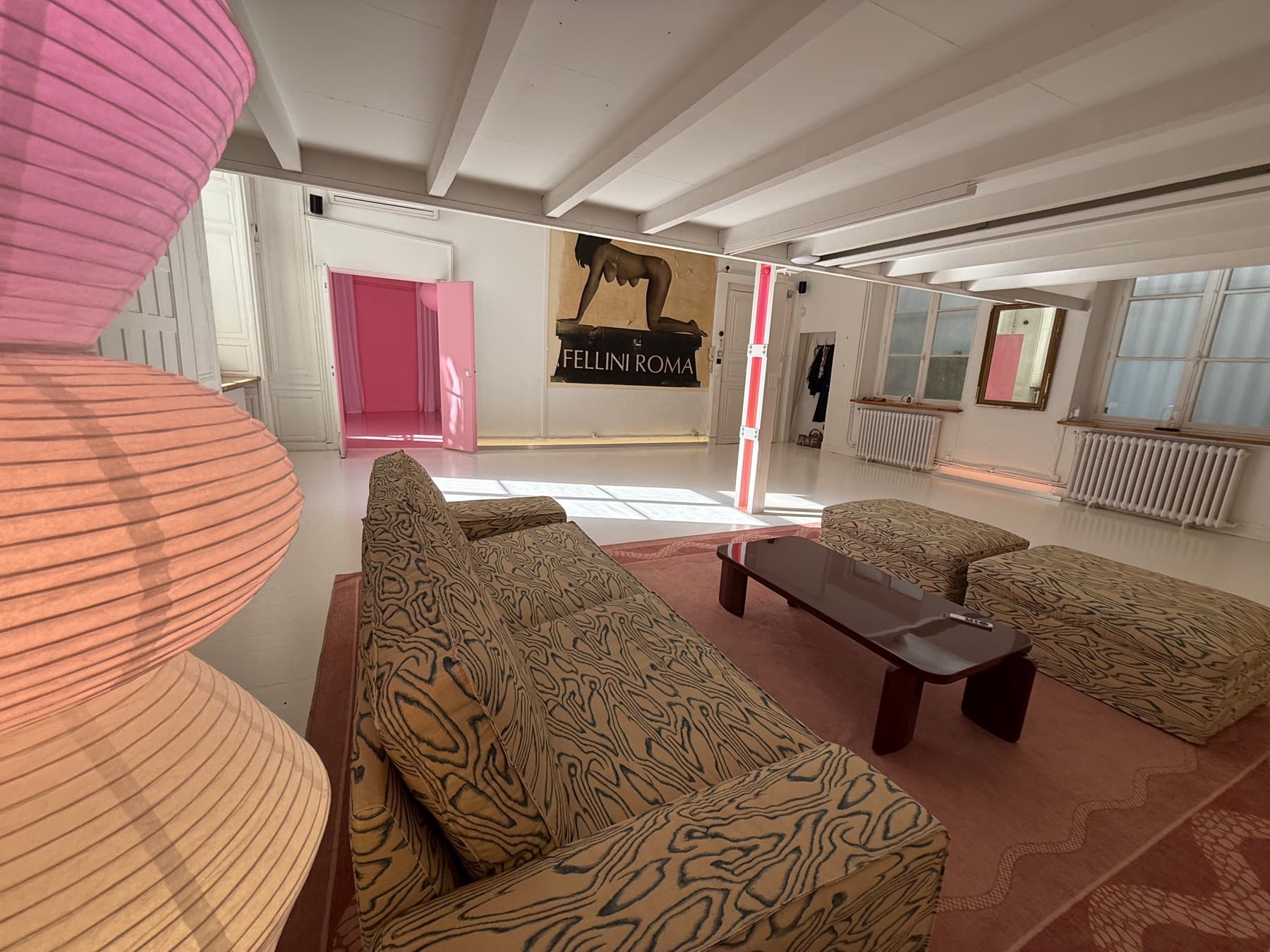 Panoramic view of the lounge — pink lamps, sofas, Fellini poster and pink apartment door