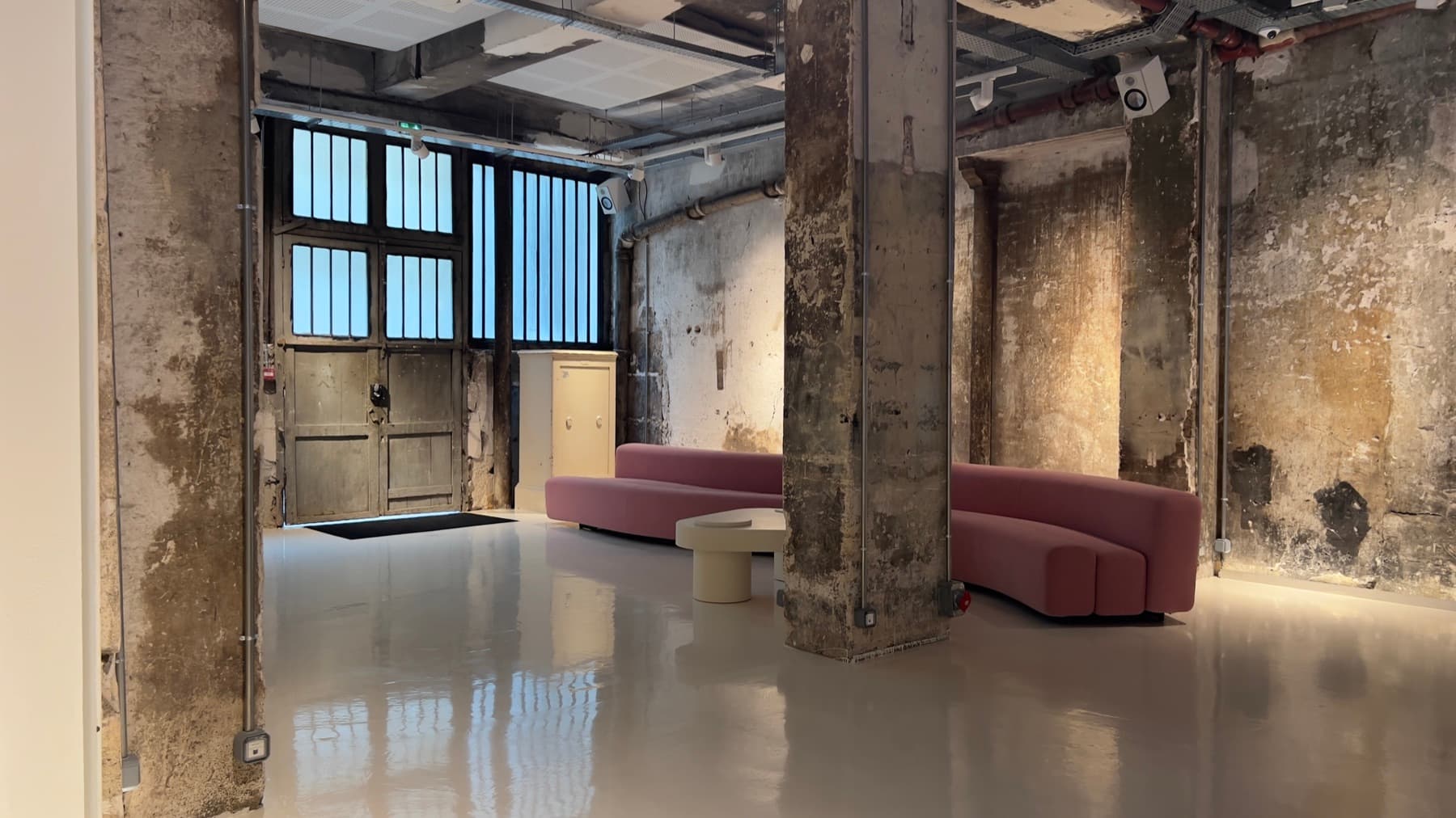 Curved pink sofa and raw industrial walls — lounge area at Chez Les Plombiers, Paris 1st