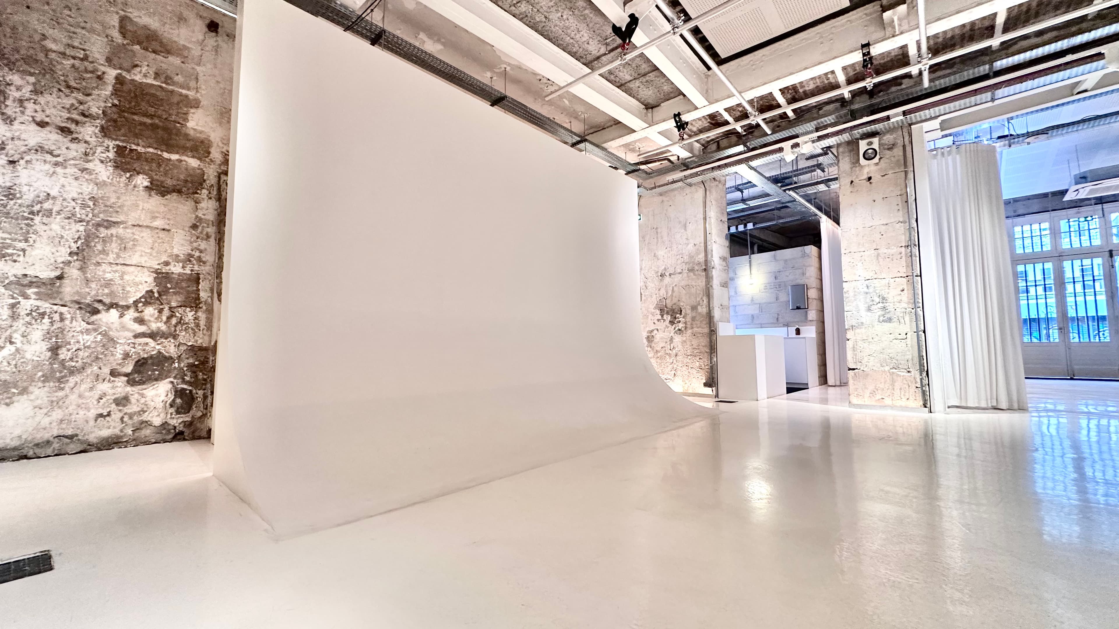 Studio photo avec mur cyclorama blanc et grille technique au plafond — Chez Les Plombiers Paris 1er