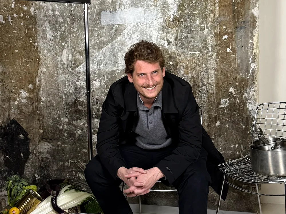 Mathias Rouveure assis devant un mur brut de L'Atelier, ses casseroles et ses légumes autour de lui